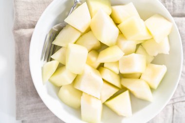 Beyaz bir kasede dilimlenmiş altın çiğ taneli kavun..