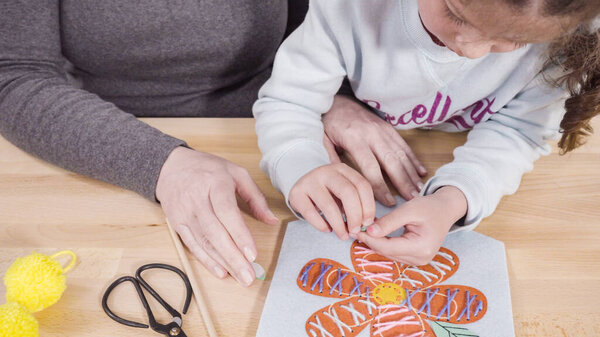 Маленькая девочка учится шить со своей матерью за рабочим столом.