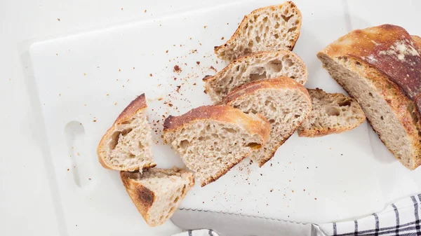 Flat lay. Slicing freshly baked sourdough wheat bread on a white cutting board.