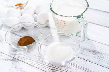 Ahşap bir masada yumurtalı ekmek hazırlamak için cam karıştırma kabındaki malzemeler..