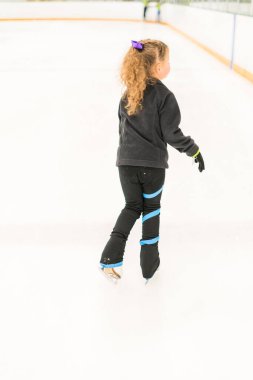 Küçük artistik patinajcı kapalı bir buz arenasında pratik yapıyor..