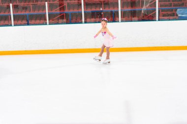 Güzel pembe elbiseli, çiçekli küçük bir kız buz pateni pistinde artistik patinaj yapıyor..