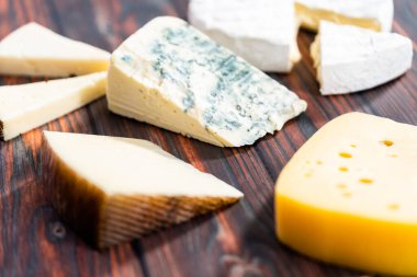 Koyu ahşap arka planda büyük gurme peynir dilimleri var..