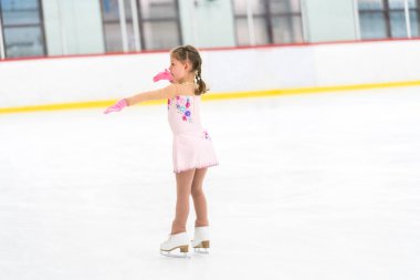 Küçük kız buz pateni pistinde artistik patinaj yapıyor..