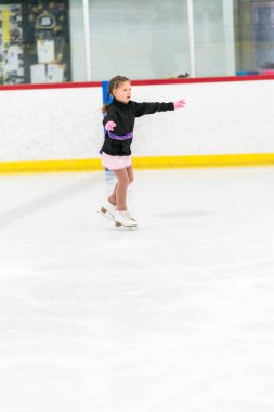 Küçük kız buz pateni pistinde artistik patinaj yapıyor..