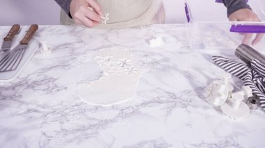 Adım adım. Mermer tezgahın üzerindeki beyaz fondanla kar tanelerini keserek..