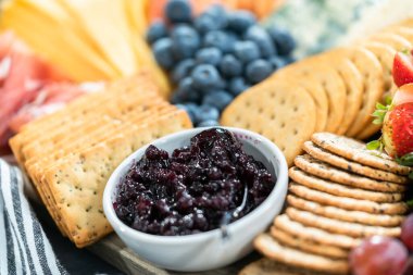 Aperatif olarak sunulan tahtanın üzerinde gurme peyniri, kraker ve meyve var..