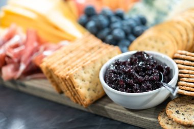 Aperatif olarak sunulan tahtanın üzerinde gurme peyniri, kraker ve meyve var..