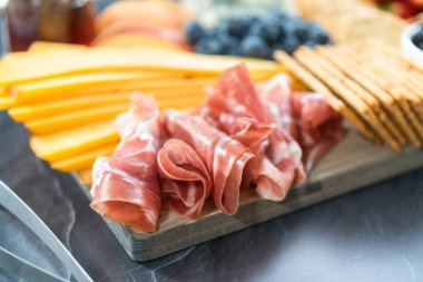 Aperatif olarak sunulan tahtanın üzerinde gurme peyniri, kraker ve meyve var..