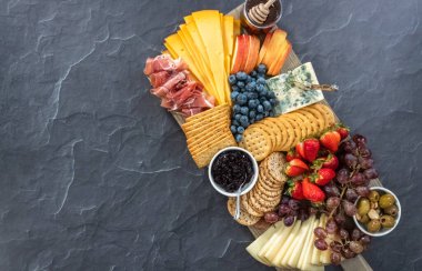 Düz yatıyordu. Aperatif olarak sunulan tahtanın üzerinde gurme peyniri, kraker ve meyve var..