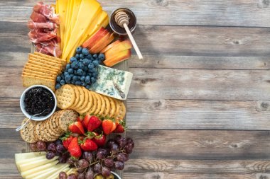 Düz yatıyordu. Aperatif olarak sunulan tahtanın üzerinde gurme peyniri, kraker ve meyve var..