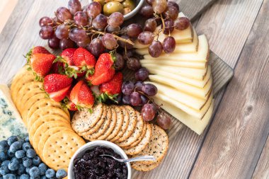 Düz yatıyordu. Aperatif olarak sunulan tahtanın üzerinde gurme peyniri, kraker ve meyve var..