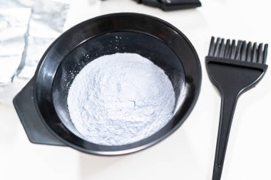 Siyah plastik bir kasede beyaz arka planda saç boyası tozu..