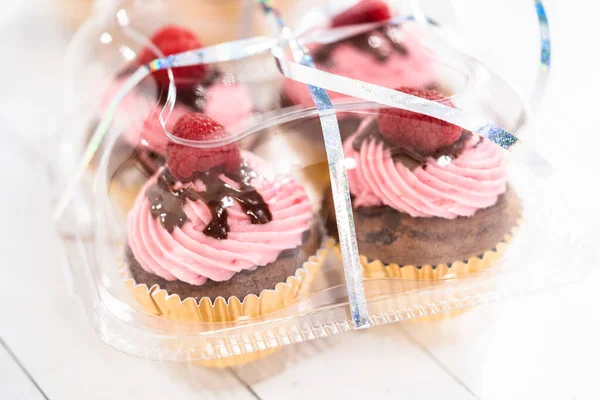 Packaging gourmet chocolate raspberry cupcakes into clear plastic boxes.