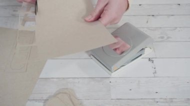 Adım adım. Kahverengi kağıttan hediye etiketlerini kağıt punçla kesiyor..