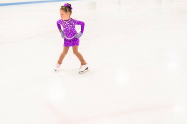 Mor elbiseyle buz pateni pistinde kristallerle buz pateni antrenmanı yapan küçük bir kız..