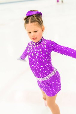 Mor elbiseyle buz pateni pistinde kristallerle buz pateni antrenmanı yapan küçük bir kız..