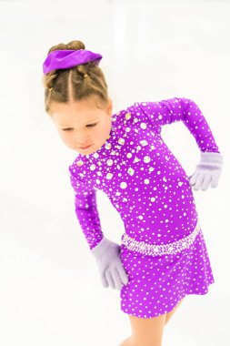 Mor elbiseyle buz pateni pistinde kristallerle buz pateni antrenmanı yapan küçük bir kız..