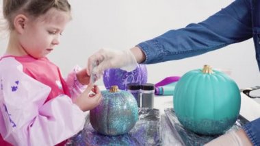 Küçük kız Cadılar Bayramı balkabağını ışıltıyla süslüyor..