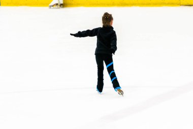 Siyah elbiseli küçük artistik patinajcı, kapalı buz arenasında pratik yapıyor..