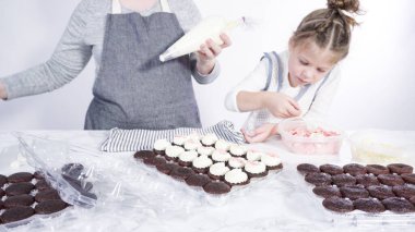 Adım adım. Küçük kız çikolatalı kekleri çikolatalı kar taneleriyle süslemeye yardım ediyor..