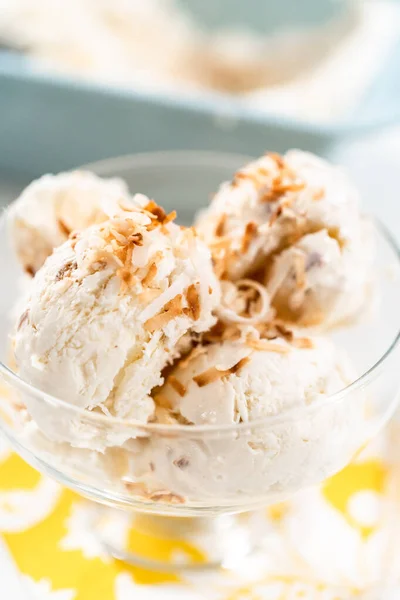 Homemade coconut ice cream garnished with roasted coconut flakes in a glass ice cream bowl.