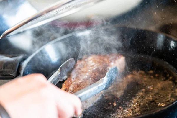 電気ストーブの上に鋳鉄フライパンでニューヨークストリップステーキをフライ — ストック写真
