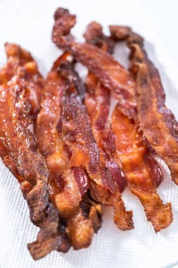 Beyaz tepside pişmiş pastırma şeritleri ve kağıt havlu..