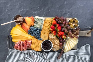 Düz yatıyordu. Aperatif olarak sunulan tahtanın üzerinde gurme peyniri, kraker ve meyve var..