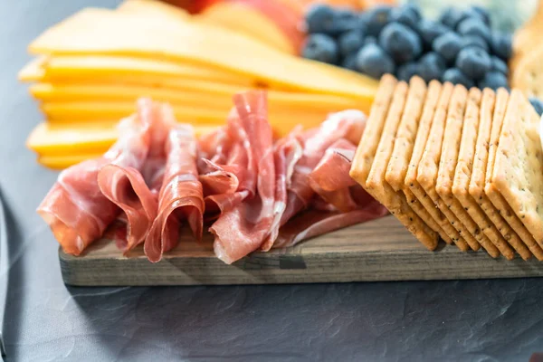 Aperatif olarak sunulan tahtanın üzerinde gurme peyniri, kraker ve meyve var..