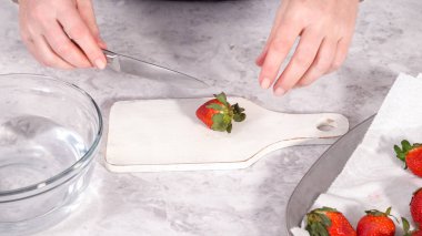 Adım adım. Beyaz bir kesme tahtasının üzerinde taze organik çilek dilimliyorum..