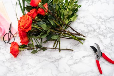 Düz yatıyordu. Çiçek buketleri düzenlemek için küçük makasla kırmızı güller buduyor..