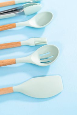 Mavi arka planda ahşap saplı yeni mavi silikon mutfak aletleri..