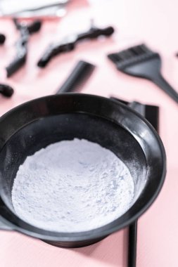 Siyah plastik bir kasede pembe arka planda saç boyası tozu..