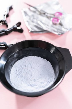 Siyah plastik bir kasede pembe arka planda saç boyası tozu..