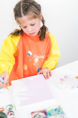 Evde akrilik boyalı bir sanat projesi üzerinde çalışan küçük bir kız..