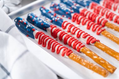 Homemade chocolate-covered pretzel rods decorated like the American flag drying on a baking sheet lined with parchment paper. clipart