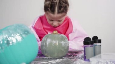 Küçük kız Cadılar Bayramı balkabağını ışıltıyla süslüyor..