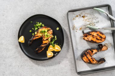 Düz yatıyordu. Siyah tabakta yeşil soğanla süslenmiş ızgara somon bifteği..