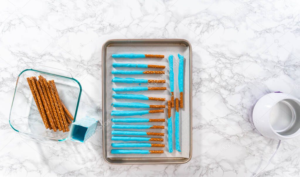 Dipping in pretzel rods into melted chocolate to prepare mermaid chocolate pretzel rods.