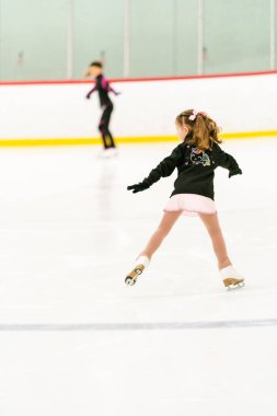 Küçük kız buz pateni pistinde artistik patinaj yapıyor..