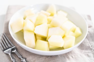 Beyaz bir kasede dilimlenmiş altın çiğ taneli kavun..