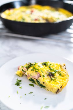 Beyaz bir yemek tabağında ıspanak ve jambonlu frittata..