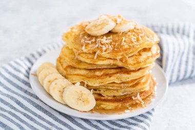 Dilimlenmiş muz, kızarmış hindistan cevizi ve akçaağaç şurubuyla süslenmiş taze hindistan cevizli krep yığını..
