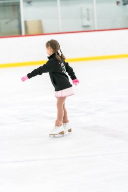 Küçük kız buz pateni pistinde artistik patinaj yapıyor..