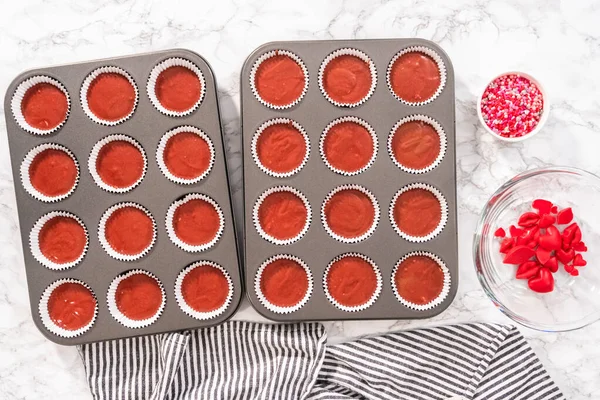 Flat lay. Flat lay. Scooping cupcake batter into a cupcake pan to bake red velvet cupcakes.