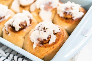 Taze pişmiş tarçınlı rulo, beyaz kremalı, mavi bir tavada..