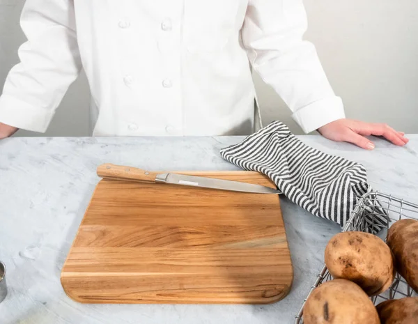 Cutting russet potatoes into wedges on wood cutting board to bake in the oven.