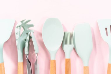 Pembe arka planda ahşap saplı yeni mavi silikon mutfak aletleri..