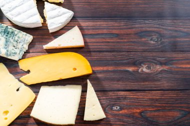 Düz yatıyordu. Koyu ahşap arka planda büyük gurme peynir dilimleri var..